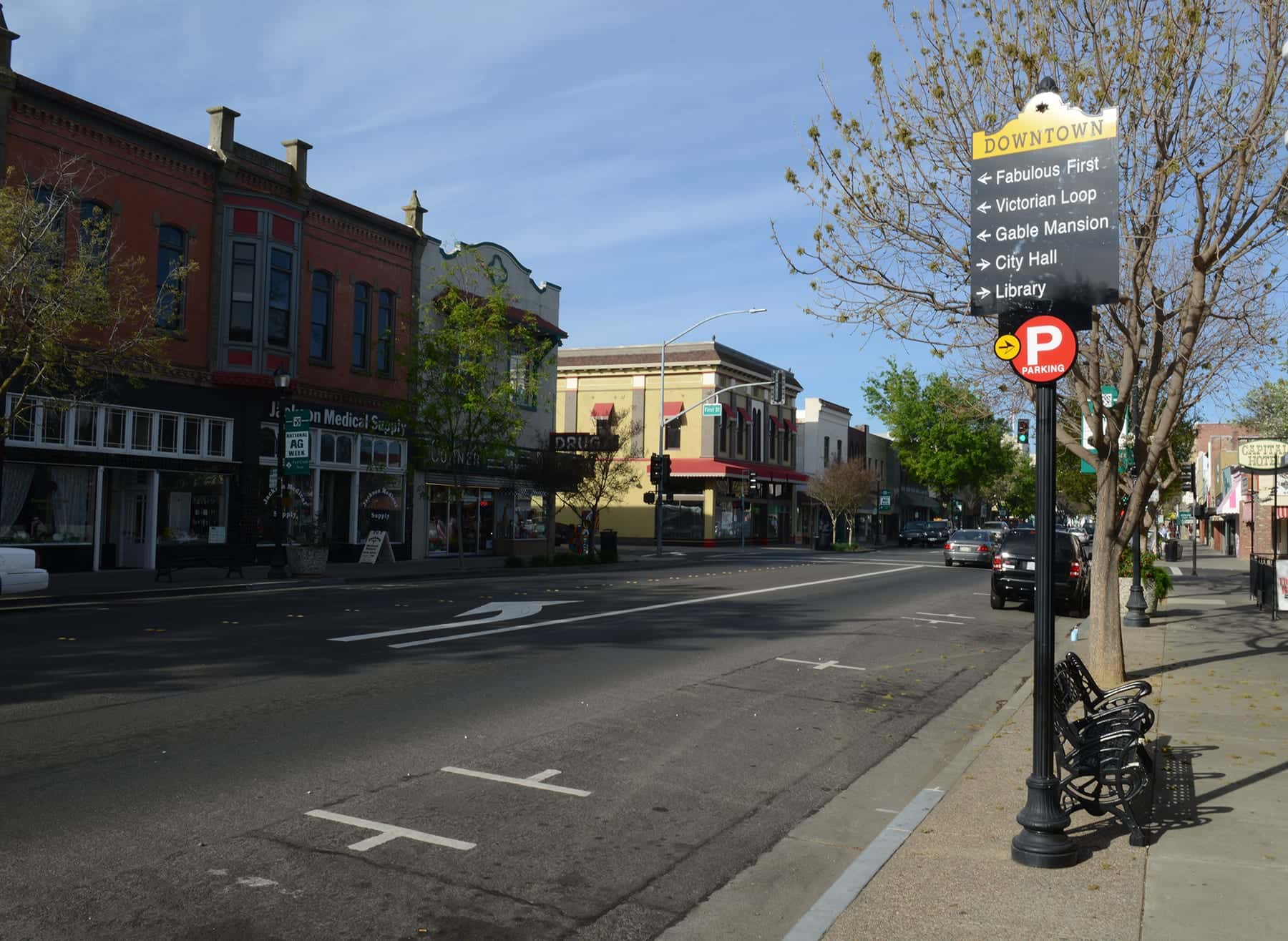 Main Street at First Street in downtown Woodland — an ornate red-brick Victorian block, a wide empty roadway and a downtown wayfinding sign