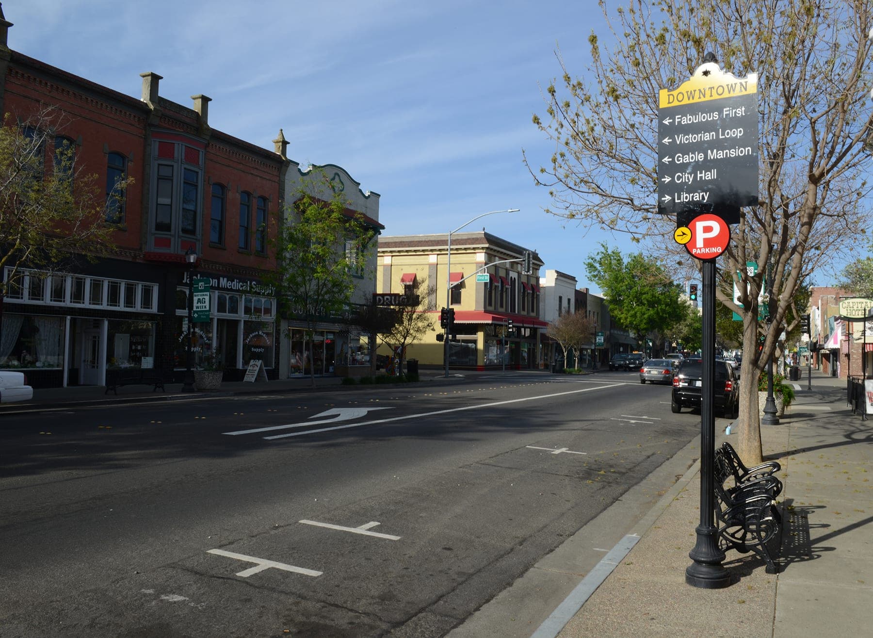 Main Street at First Street in downtown Woodland — an ornate red-brick Victorian block, a wide empty roadway and a downtown wayfinding sign