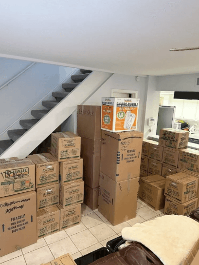A hallway and staircase packed into labelled cartons, with tall flat boxes for mirrors and pictures standing against the wall