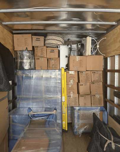 The inside of a loaded truck: cartons stacked to the roof, a shrink-wrapped sofa along one wall and a ladder strapped down the middle