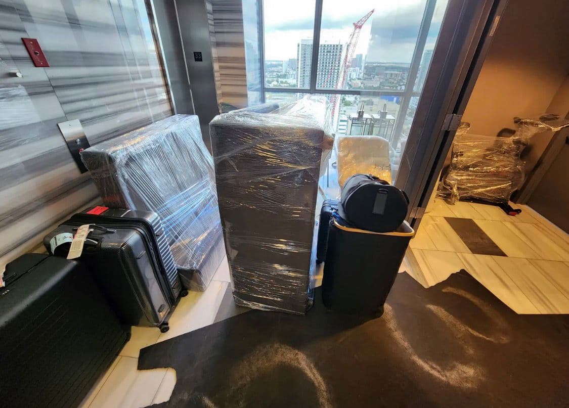 A lift lobby staged for loading: runners down over the stone floor, every piece shrink-wrapped and standing clear of the walls