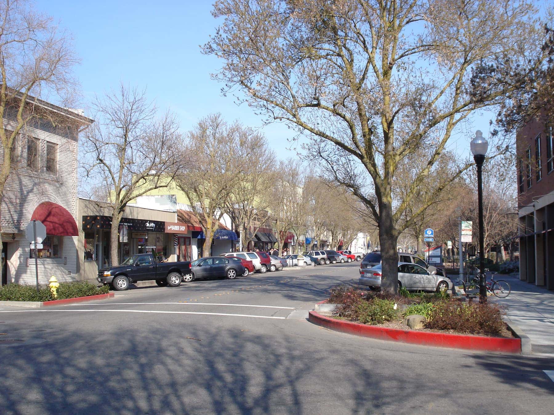 G Street in downtown Davis in winter — bare plane trees, one- and two-storey shopfronts and cars angle-parked down both kerbs
