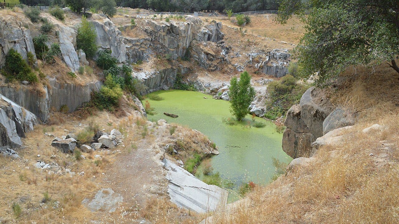 The old California Granite Company quarry in Rocklin: cut granite walls around a green pool, oaks along the rim